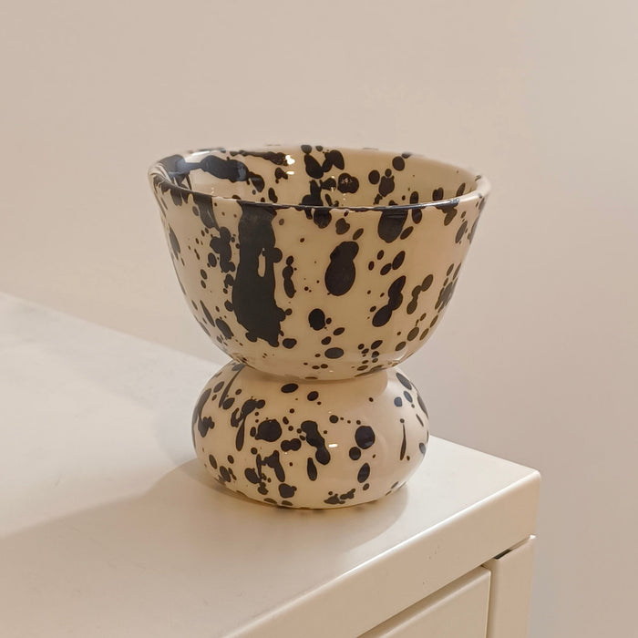 A ceramic pedestal cup with a black speckled pattern