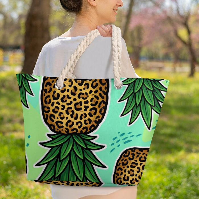 A woman outdoors carrying a large tote bag with a tropical pineapple print featuring leopard-print centers and green leaves on a mint background.