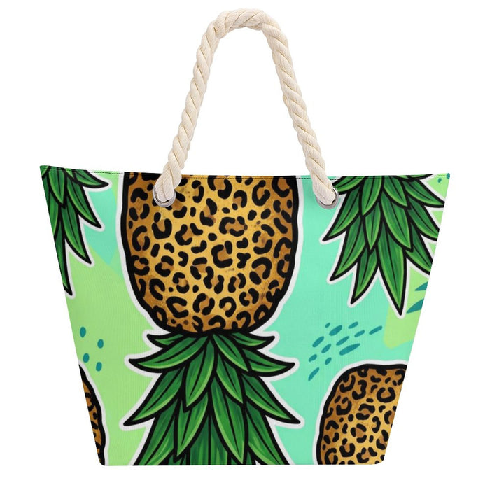A beach tote bag featuring a bold pattern of stylized pineapples with leopard print bodies and green leaves on a light mint background, complete with thick cream rope handles.